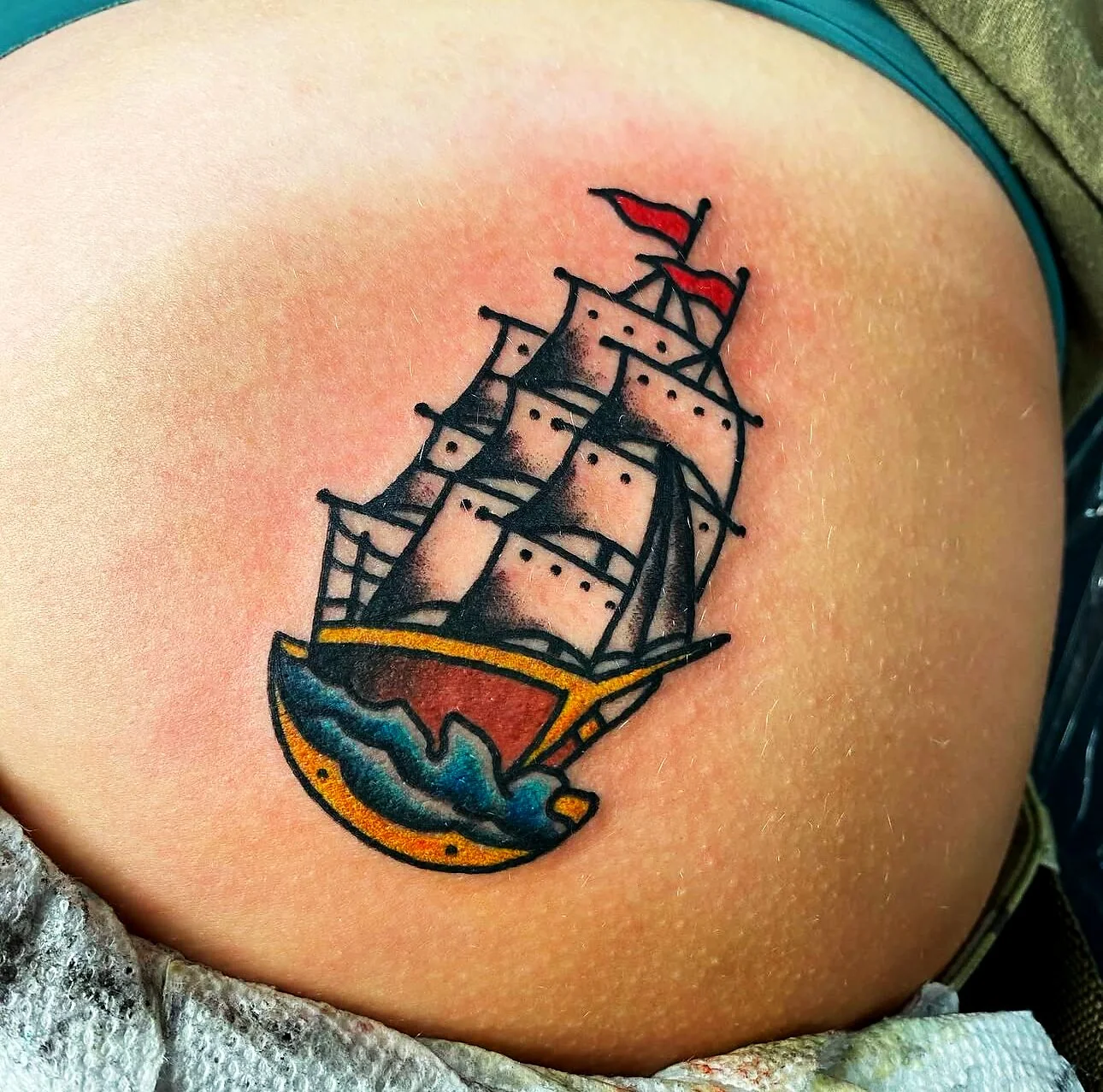 American Traditional sailing ship with red flag tattoo on hip by 2bit (Chris Curren) at Lost at Sea Tattoo, Chinatown, Honolulu