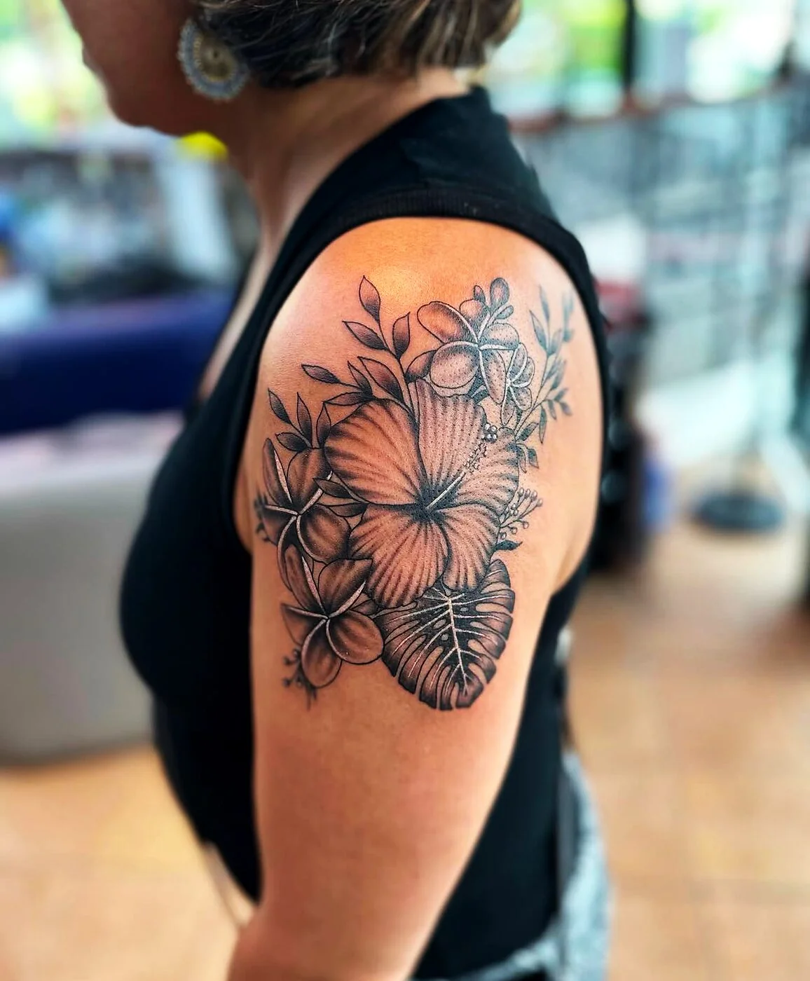 Black & Grey hibiscus, plumeria and monstera bouquet tattoo on shoulder by 2bit (Chris Curren) at Lost at Sea Tattoo, Chinatown, Honolulu