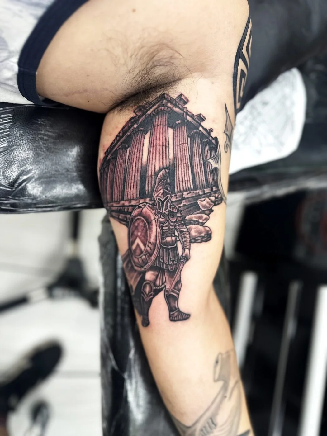 Black & Grey Spartan warrior with shield in front of Greek temple tattoo on bicep by 2bit (Chris Curren) at Lost at Sea Tattoo, Chinatown, Honolulu