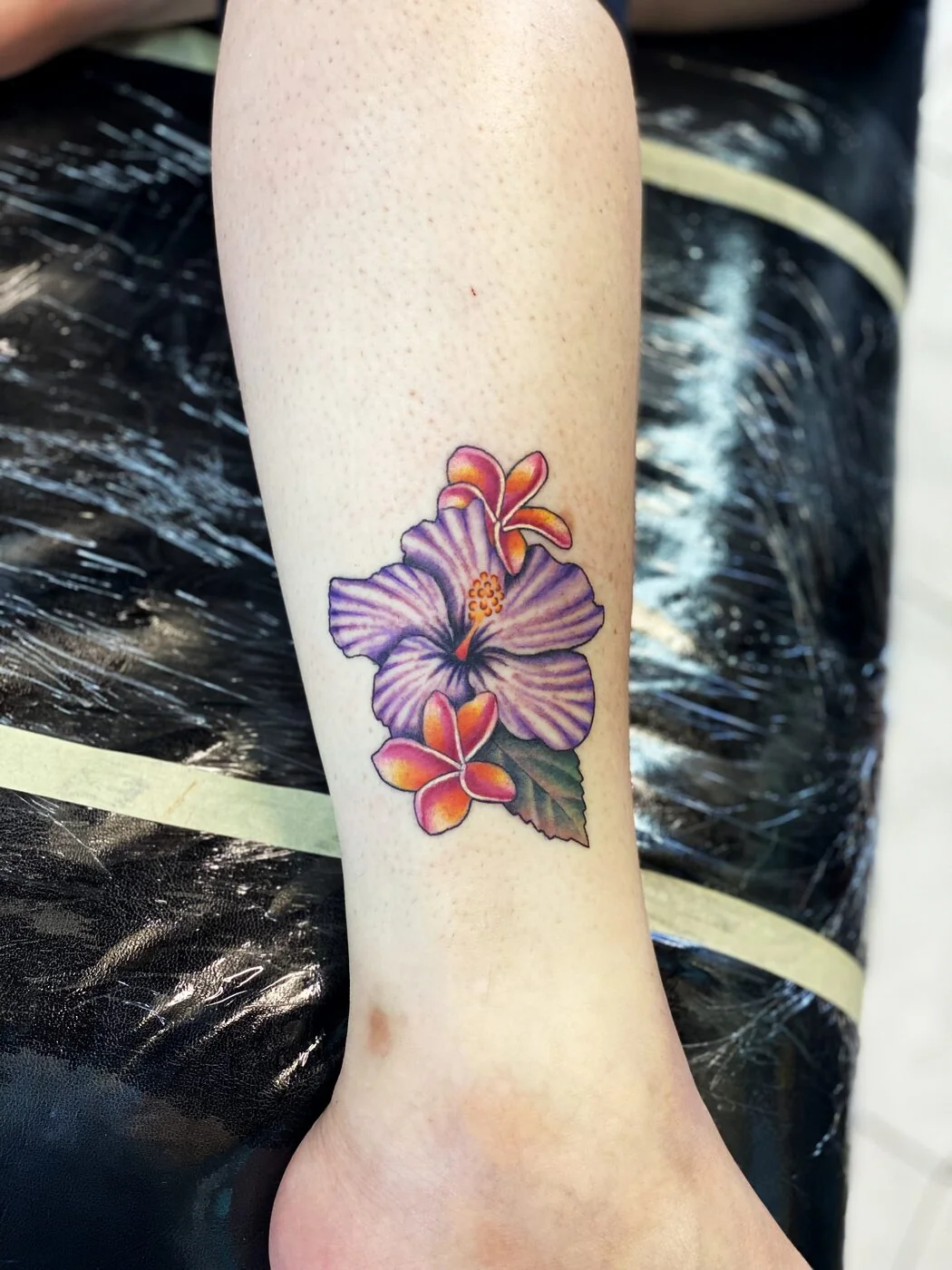 Color Realism purple hibiscus and plumeria tattoo on ankle by 2bit (Chris Curren) at Lost at Sea Tattoo, Chinatown, Honolulu