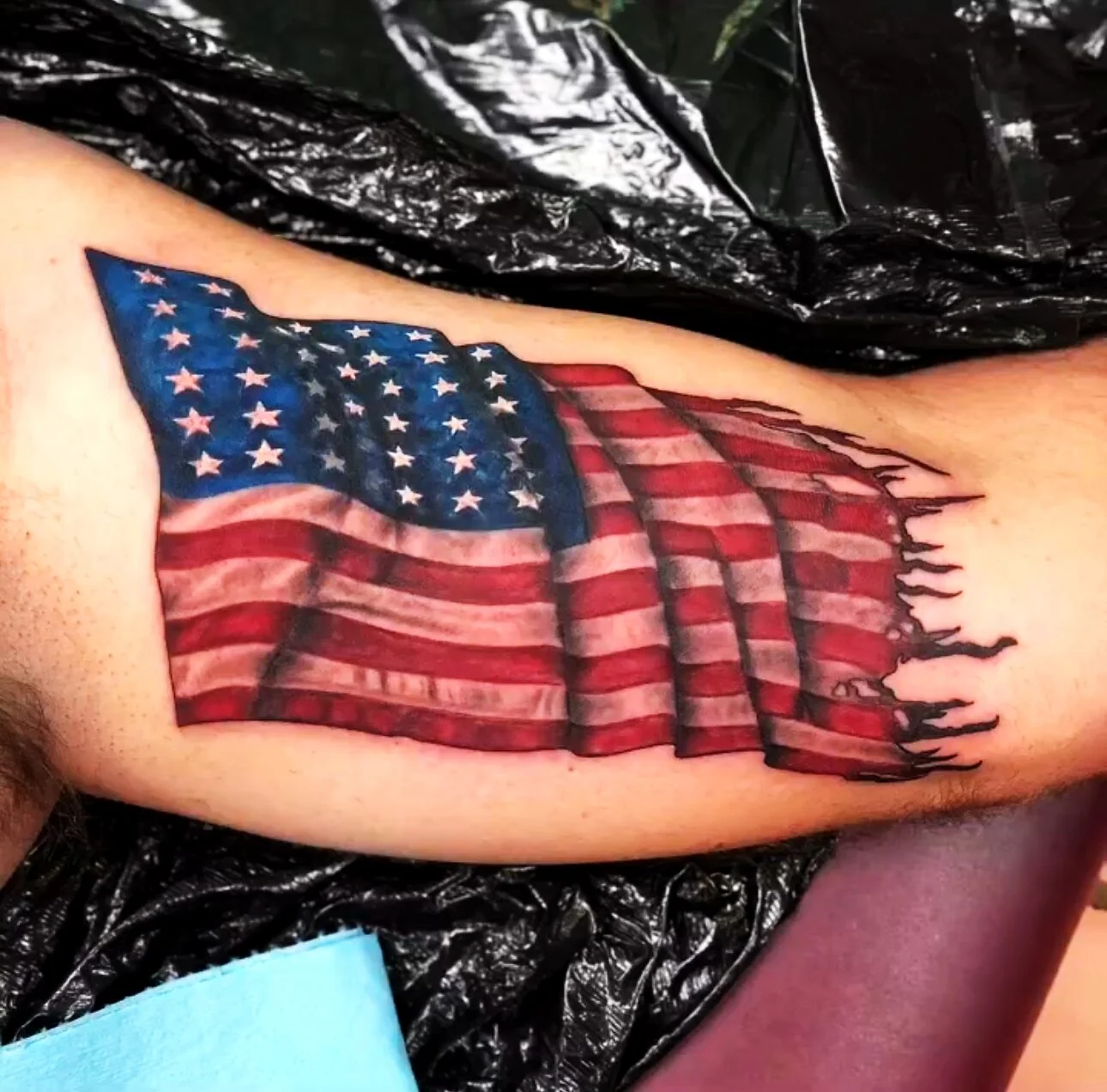 Color Realism tattered American flag tattoo on bicep by 2bit (Chris Curren) at Lost at Sea Tattoo, Chinatown, Honolulu